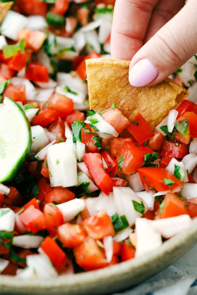 Pico de Gallo is a made from scratch salsa that is loaded with bold flavors from jalapeno, lime, cilantro, and juicy chunks of tomato and onion. One dip will certainly not be enough and you will be scraping the bottom of the bowl in no time! Dipping a chip into fresh pico de gallo.