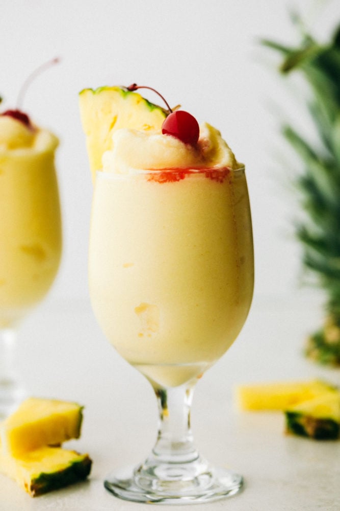 This Pina Colada is a sweet, creamy, frozen drink bursting with fruity flavors from pineapple and coconut. The flavors are so vibrant, they will transport you from your porch to a lounge chair at a tropical beach! Pina colata garnished with cherry and pineapple slice.