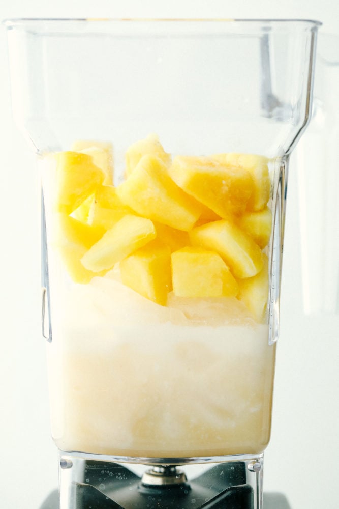 This Pina Colada is a sweet, creamy, frozen drink bursting with fruity flavors from pineapple and coconut. The flavors are so vibrant, they will transport you from your porch to a lounge chair at a tropical beach! Pina Colada ingredients in a blender ready to be mixed.