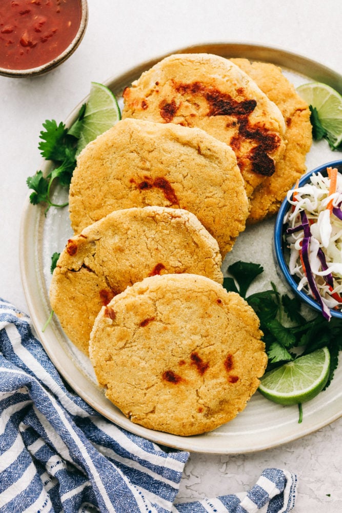 Easy Bean and Cheese Pupusas are handmade griddle cakes filled with savory beans and cheese. They are cheap and easy to make, but just beware because they are addicting! Easy Bean and Cheese Pupusas on a plate served with slaw and salsa.