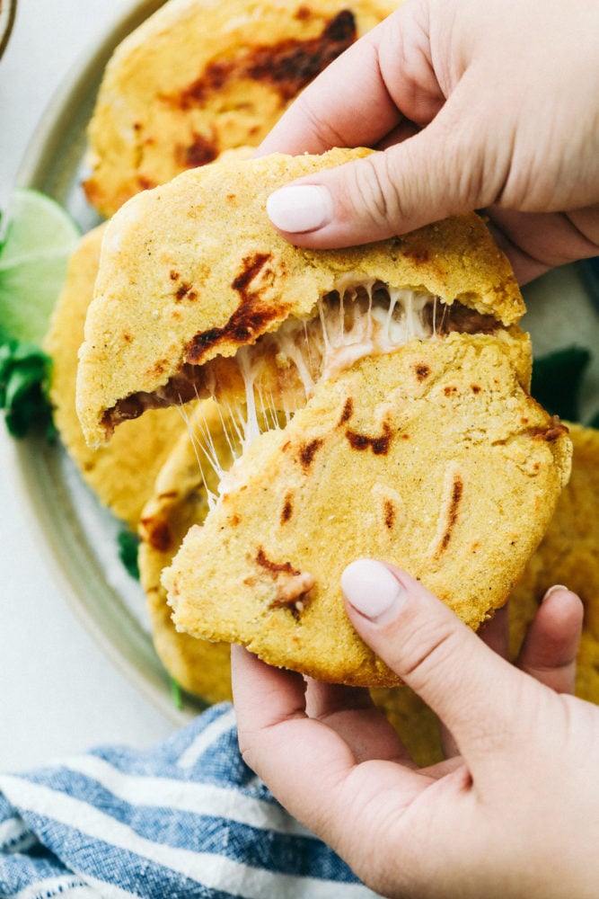Easy Bean and Cheese Pupusas are handmade griddle cakes filled with savory beans and cheese. They are cheap and easy to make, but just beware because they are addicting! Easy Bean and Cheese Pupusas being ripped into two pieces to reveal gooey cheese inside.