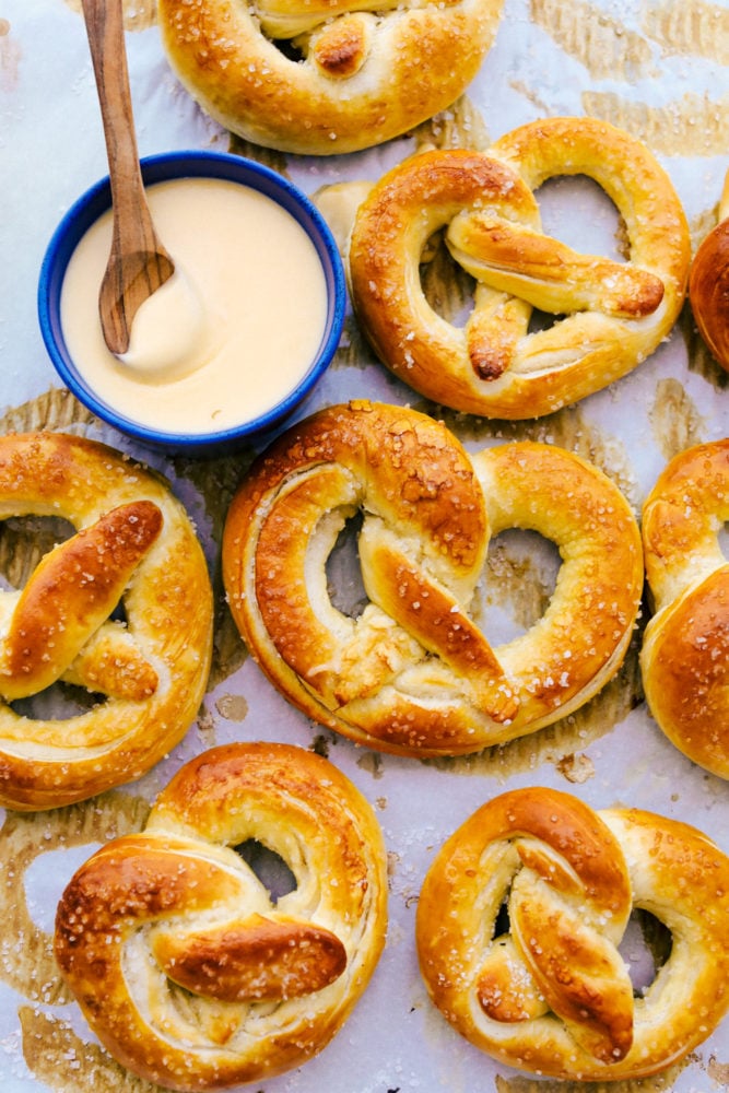 Baked Soft Pretzels are soft and chewy on the inside with the perfect salty golden exterior.ย This recipe will walk you through these easy homemade pretzels with step by step instructions! Finished soft pretzels with cheese dip in a blue bowl.