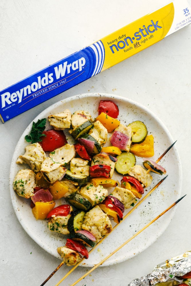 Garlic Ranch Chicken Skewers are the perfect way to enjoy kabobs this summer. Get grilling with this easy to make chicken that has all the flavor on each skewer! Chicken and vegetables on a white plate with Reynolds wrap box on the side.