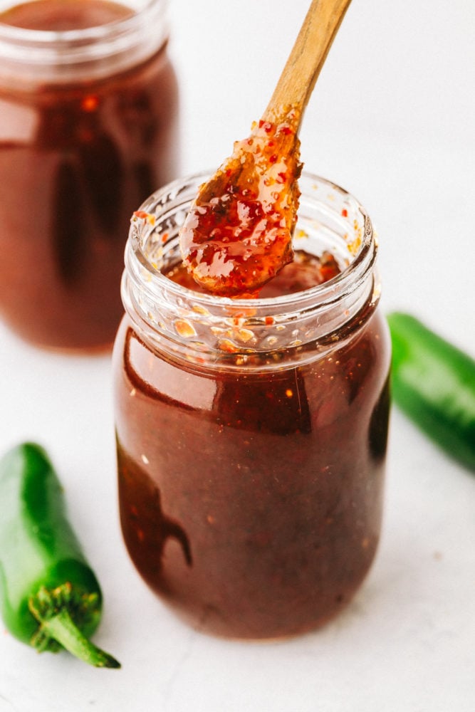 Homemade Jalapeño Jelly is a perfect sweet and spicy combination you will want to slather on everything. It will become a staple in your fridge or freezer from now on! Dipping jalapeño jelly out of a glass mason jar.