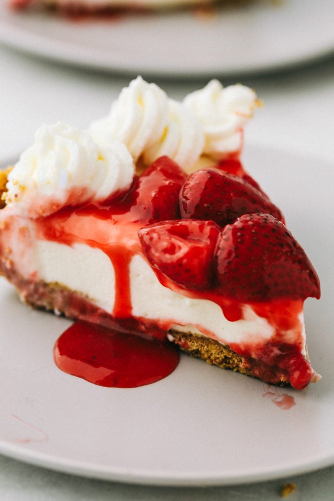 No Bake Cheesecake is so creamy, luxurious, and surprisingly easy to make from scratch at home.ย Top it with whipped cream and fresh fruit and it will be a huge hit that everyone will obsess over! Finished no bake cheese cake topped with whipped cream strawberry syrup and strawberries.