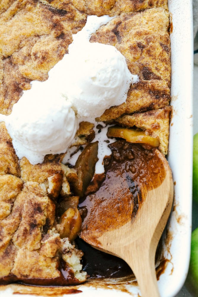 Old Fashioned Apple Cobbler is a warm baked fruit dessert that is topped with a perfect biscuit-like crust.ย The warm cinnamon spice is comforting and satisfying and nails a perfect summer dessert! Scooping apple cobbler and vanilla ice cream out of a white baking dish.