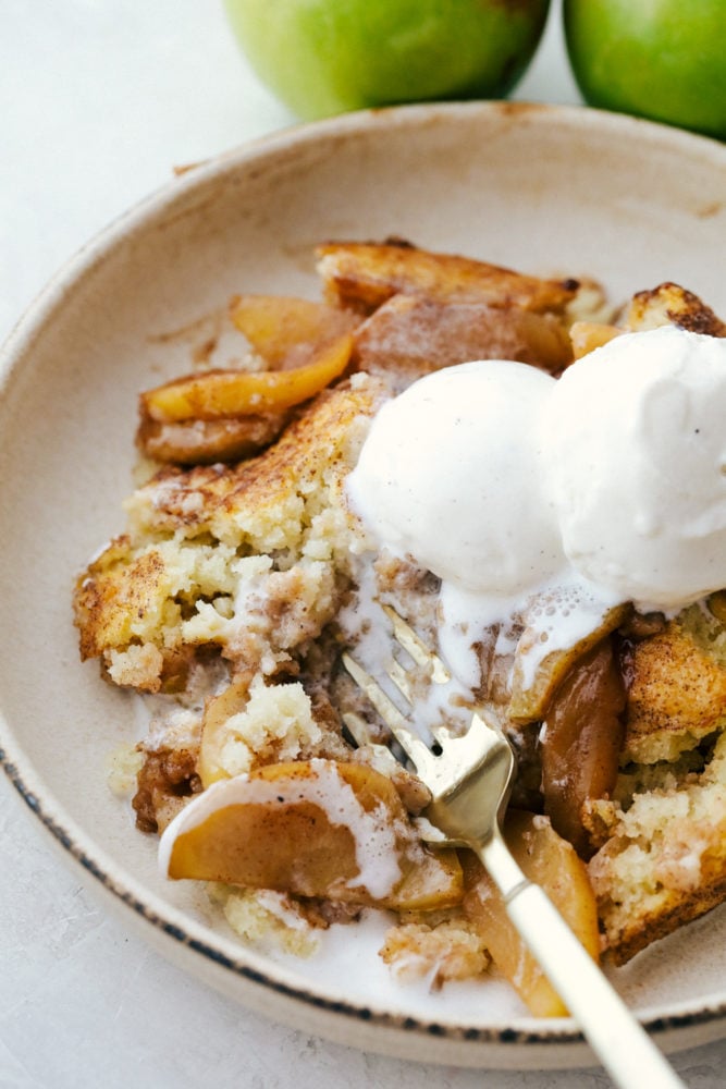 Old Fashioned Apple Cobbler is a warm baked fruit dessert that is topped with a perfect biscuit-like crust.ย The warm cinnamon spice is comforting and satisfying and nails a perfect summer dessert! Apple cobbler on a plate topped with vanilla ice cream.