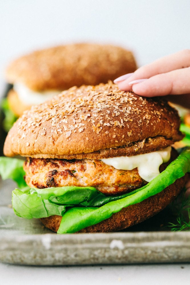 Salmon Burgers are light and tasty burgers that are easy to make ahead and enjoy all summer!ย The homemade salmon patty is flavorful and quick and easy to grill! Close up on picking up a finished salmon burger.