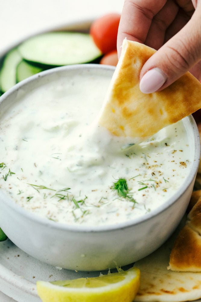 Tzatziki Sauce is a Greek inspired, yogurt-based sauce you and your family will go crazy over. It is creamy and bursting with light and refreshing cucumber, dill, and garlic flavors that will make this a Mediterranean inspired favorite this summer! Dipping a chip in Tzatziki sauce.