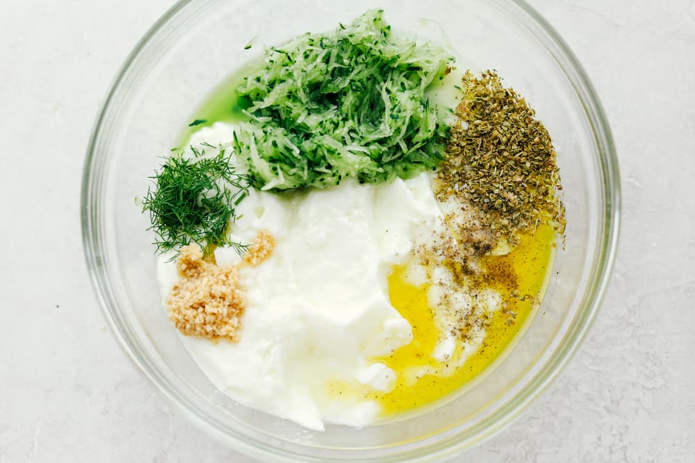 Tzatziki Sauce is a Greek inspired, yogurt-based sauce you and your family will go crazy over. It is creamy and bursting with light and refreshing cucumber, dill, and garlic flavors that will make this a Mediterranean inspired favorite this summer!Tzatziki Sauce is a Greek inspired, yogurt-based sauce you and your family will go crazy over. It is creamy and bursting with light and refreshing cucumber, dill, and garlic flavors that will make this a Mediterranean inspired favorite this summer! Ingredients for Tzatziki sauce in a clear bowl.