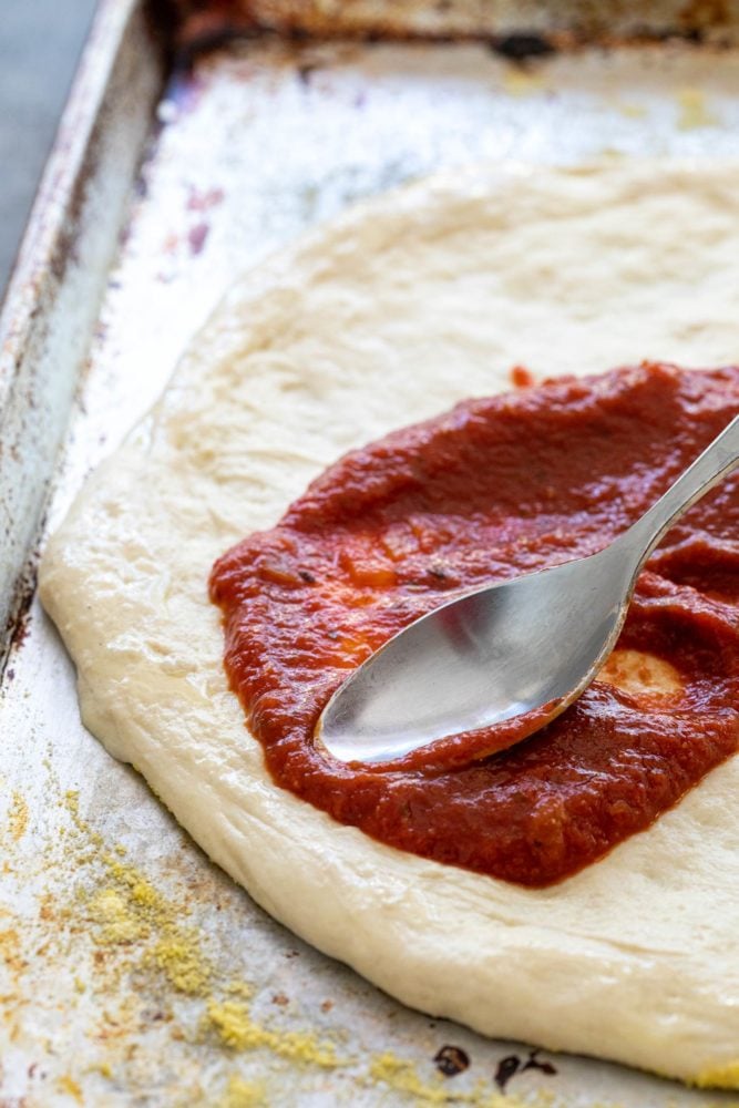 This easy zucchini pizza recipe is the perfect vegetarian meal when you're craving a slice. Fresh dough is topped with a savory red sauce, mozzarella cheese, and thin slices of zucchini. The pie is baked until the crust is crispy and cheese is hot and bubbly. Spoon spreading pizza sauce on dough