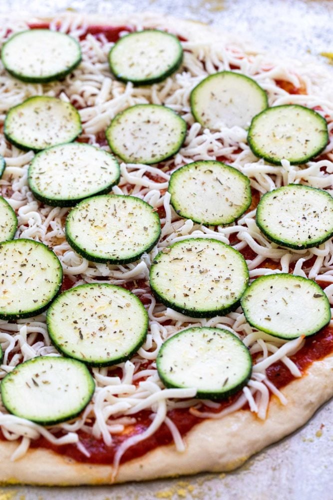 This easy zucchini pizza recipe is the perfect vegetarian meal when you're craving a slice. Fresh dough is topped with a savory red sauce, mozzarella cheese, and thin slices of zucchini. The pie is baked until the crust is crispy and cheese is hot and bubbly. Thin slices of zucchini layered on top of a pizza