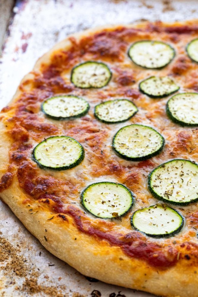 This easy zucchini pizza recipe is the perfect vegetarian meal when you're craving a slice. Fresh dough is topped with a savory red sauce, mozzarella cheese, and thin slices of zucchini. The pie is baked until the crust is crispy and cheese is hot and bubbly. Oven baked pizza with slices of zucchini on top