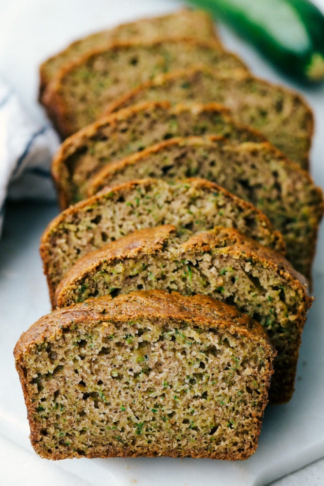 You better believe I count down to zucchini season so I know when I can make this delicious Zucchini Bread! It’s moist, perfectly spiced, and loaded with the best flavor and a hint of veggies! Zucchini bread sliced up in a photo on a white plate.