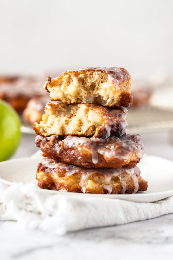 Juicy chunks of apple, coated in batter and shallow fried, these homemade apple fritters are a tender, delicious apple breakfast treat that are also incredibly simple to make. They’re topped off with an addictive but simple icing which takes them to a whole ‘nother level. A stack of apple fritters on a white plate, the top one is broken in half showing the inside.