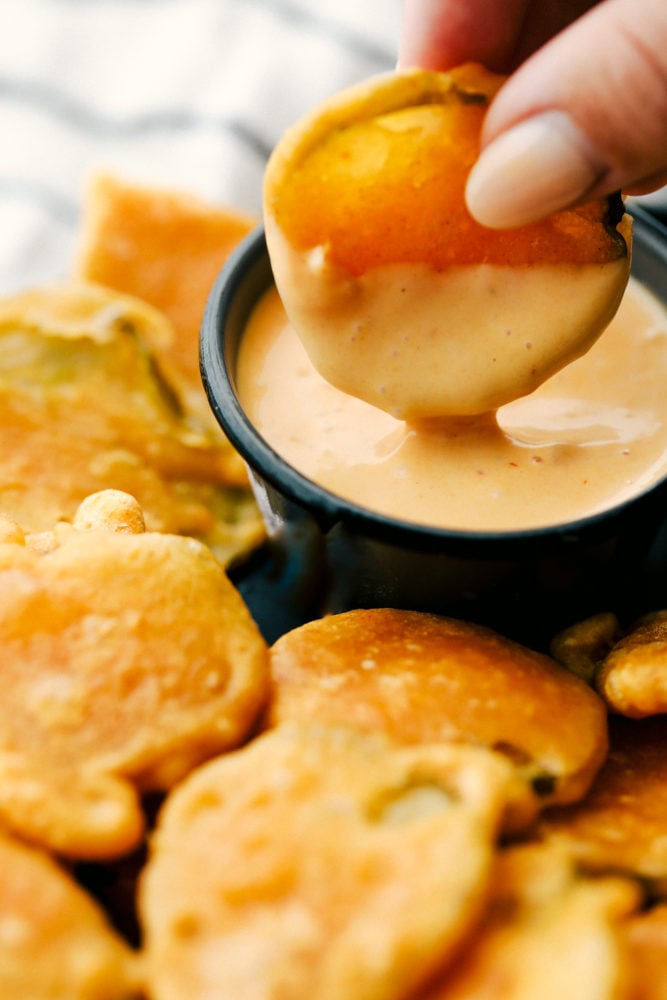 Fried Pickles are tangy dill pickles dipped in a smooth flavorful batter and fried till crispy golden brown. A sure fire winner for any appetizer or snack time! Fried pickle being dipped in a sauce dip with other fried pickles on the side.