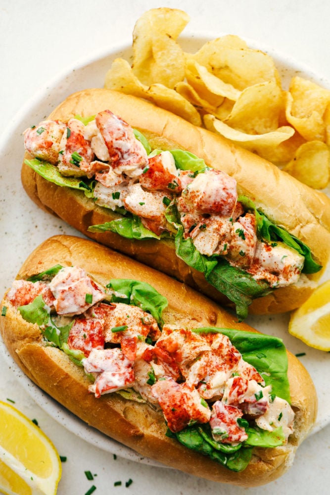 An Easy Lobster Roll is a heavenly sandwich with a soft and chewy bun that's stuffed with cool, fresh lobster salad made from a sweet mayonnaise base. Every bite is packed with crave-worthy flavor that is light and tasty! Finished lobster rolls on a white serving plate with chips.