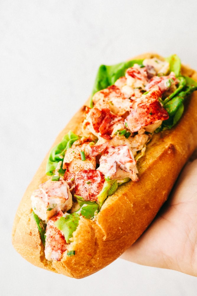 An Easy Lobster Roll is a heavenly sandwich with a soft and chewy bun that's stuffed with cool, fresh lobster salad made from a sweet mayonnaise base. Every bite is packed with crave-worthy flavor that is light and tasty! Holding a finished lobster roll.