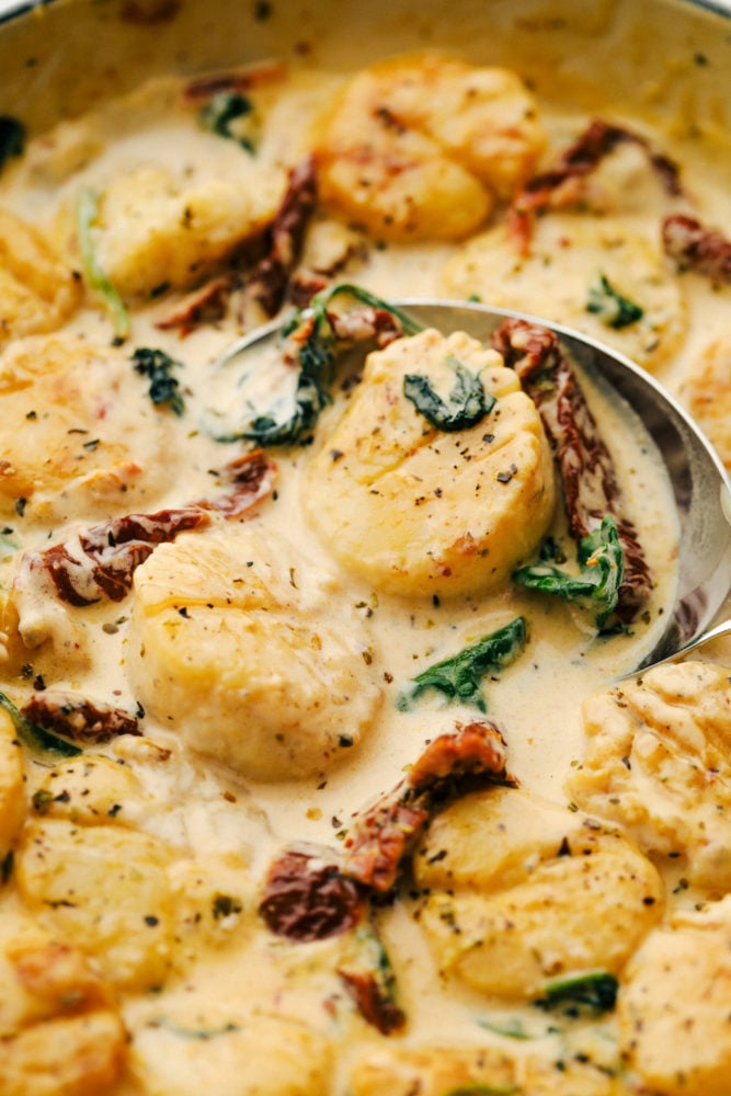 Creamy tuscan garlic scallops are infused in a savory garlic sauce that is absolutely to die for! Easy to make and filled to the brim with flavor, this is a MUST-make dinner for busy weeknights! Tuscan garlic scallops in a skillet with a spoon stirring it together.
