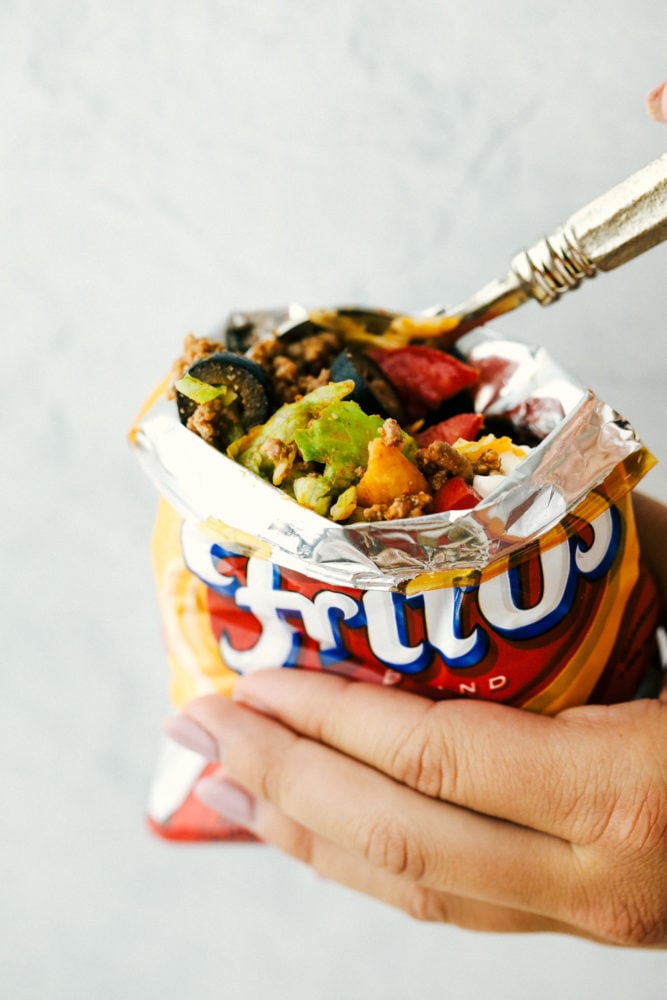 Walking Tacos are quick and easy deconstructed tacos that are made and served right in a chip bag. Great for active parties or on the go meals because they are filling and fast! Scooping a bite out of a walking taco bag.