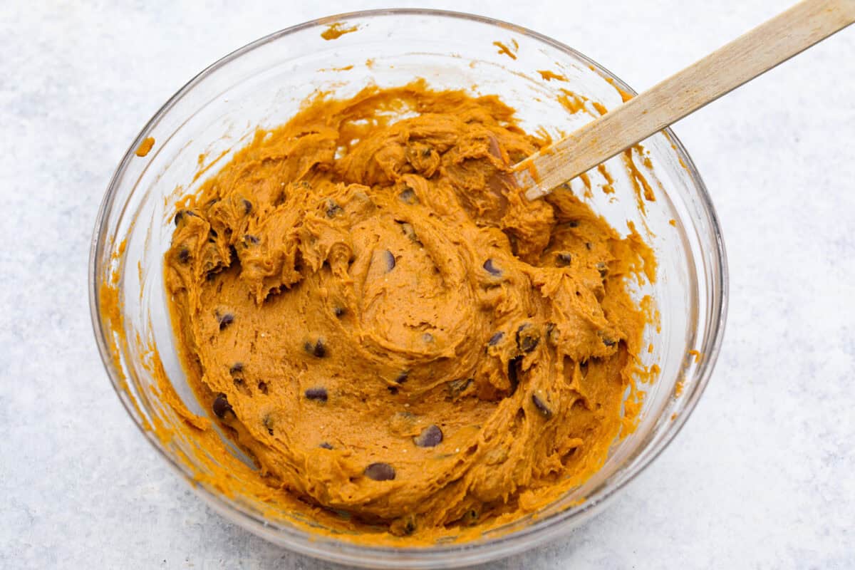 Easy as 1,2,3, these delicious pumpkin chocolate chip cookies are super quick and tasty! They are light, fluffy, and packed with pumpkin flavor and silky milk chocolate. With only three ingredients, it can’t get much easier than that! Overhead shot of chocolate chips mixed in to the puree and spiced cake mixture.
