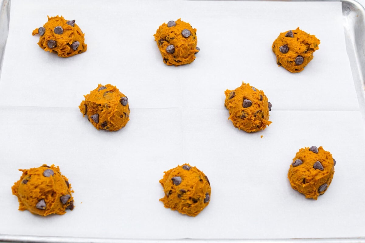 Easy as 1,2,3, these delicious pumpkin chocolate chip cookies are super quick and tasty! They are light, fluffy, and packed with pumpkin flavor and silky milk chocolate. With only three ingredients, it can’t get much easier than that! Overhead shot of scooped pumpkin chocolate chip cookie dough balls on a baking sheet.