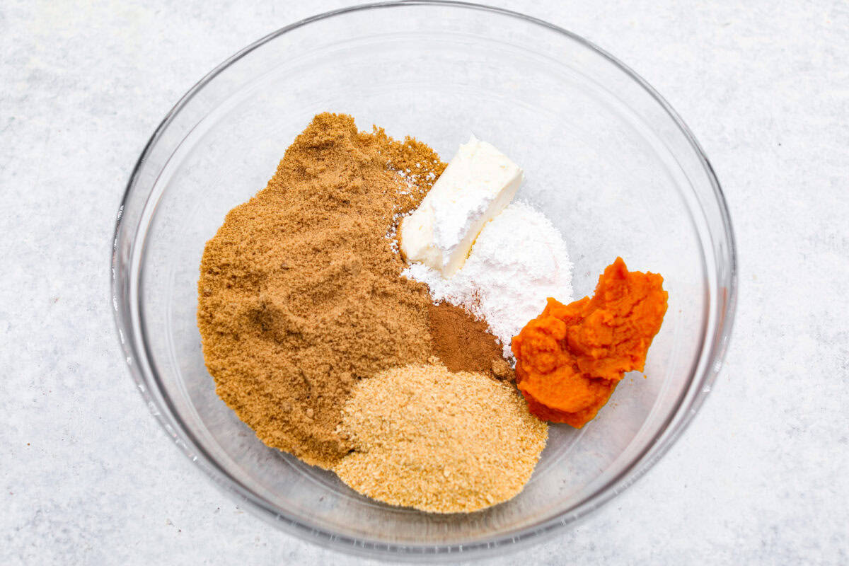 Pumpkin cream cheese truffles combine smooth cream cheese, pumpkin puree, crunchy graham cracker, and gingersnap crumbs, all dunked in sweet white chocolate. The best fall dessert. Overhead shot of pumpkin, sugar, cream cheese, graham cracker and gingersnap crumbs in a bowl.