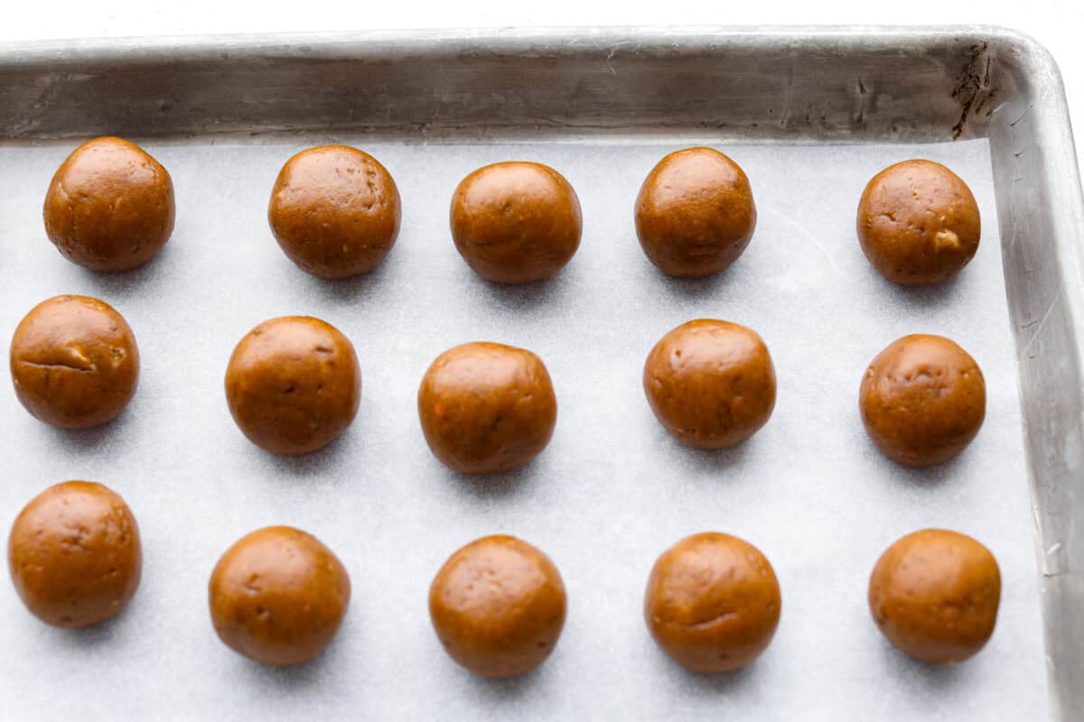 Pumpkin cream cheese truffles combine smooth cream cheese, pumpkin puree, crunchy graham cracker, and gingersnap crumbs, all dunked in sweet white chocolate. The best fall dessert. Overhead shot of rolled out truffle balls on parchment paper on a cookie sheet.