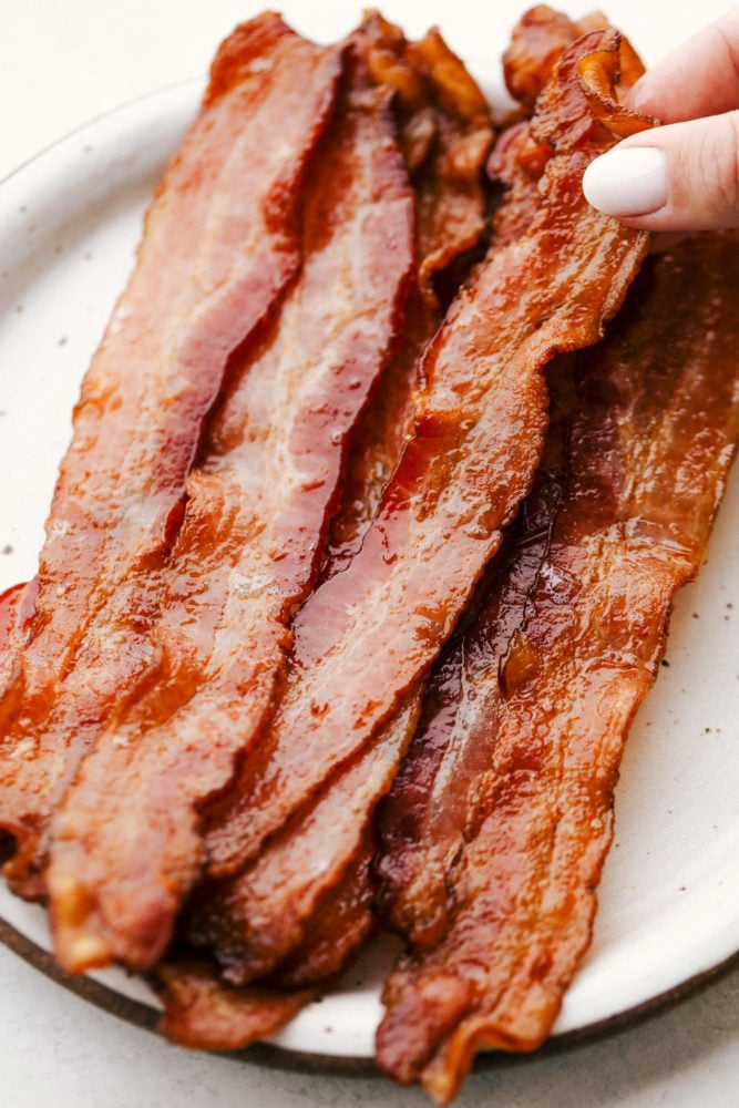 Everyone loves Bacon, and once you try baking it, you'll love it even more! It's just perfectly crisp, amazing flavor, and easy clean up. You will have bacon every morning! Crispy baked bacon on a plate.