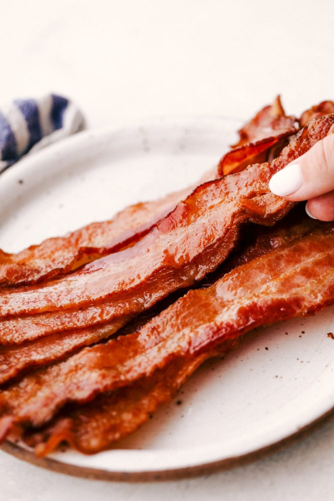 Everyone loves Bacon, and once you try baking it, you'll love it even more! It's just perfectly crisp, amazing flavor, and easy clean up. You will have bacon every morning! Perfectly Baked Crispy Bacon on a white plate.