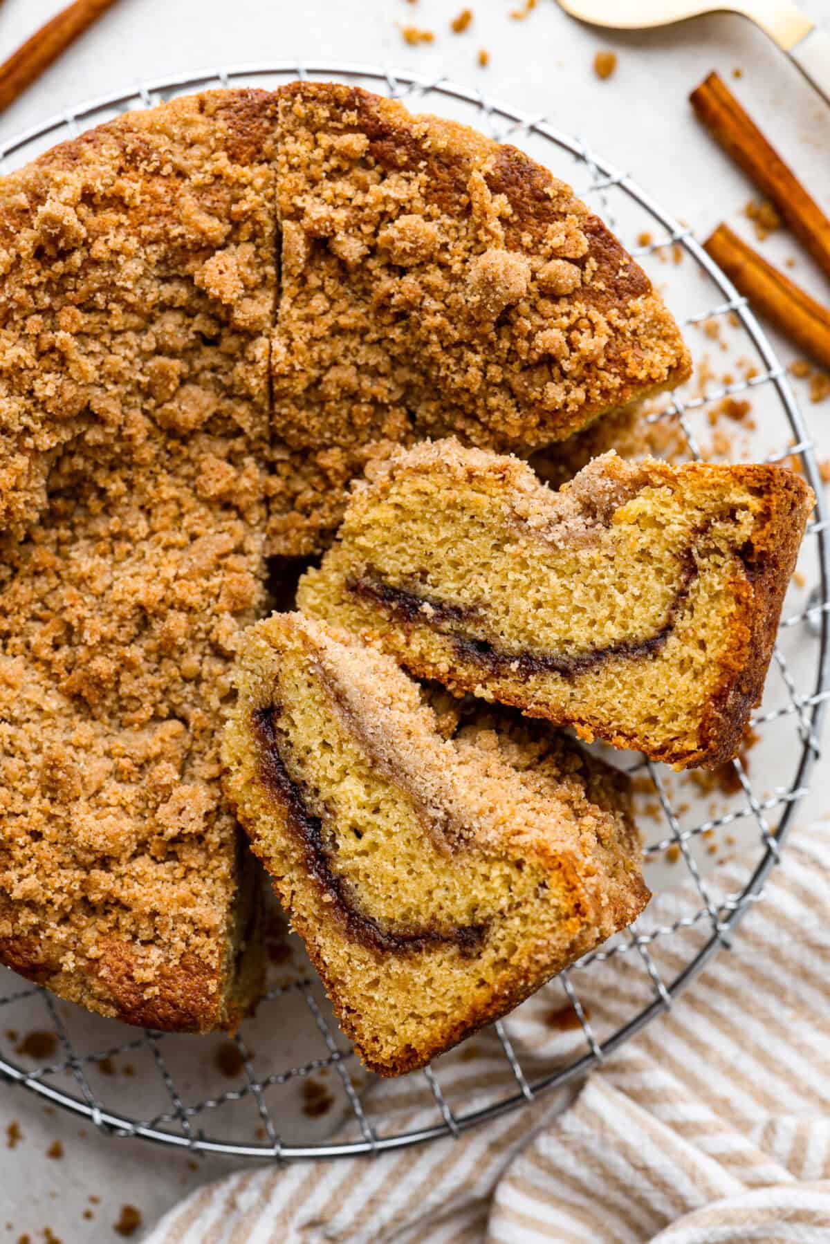 This classic cinnamon coffee cake is loaded with decadent cinnamon sugar swirls and topped with crumbly cinnamon streusel. It's the perfect treat to share at any brunch, book club, or dessert for any night of the week. The warm, satisfying aroma will fill your heart and your home! Overhead shot of completed cinnamon coffee cake with two slices on their side, all on a wire cooling rack.