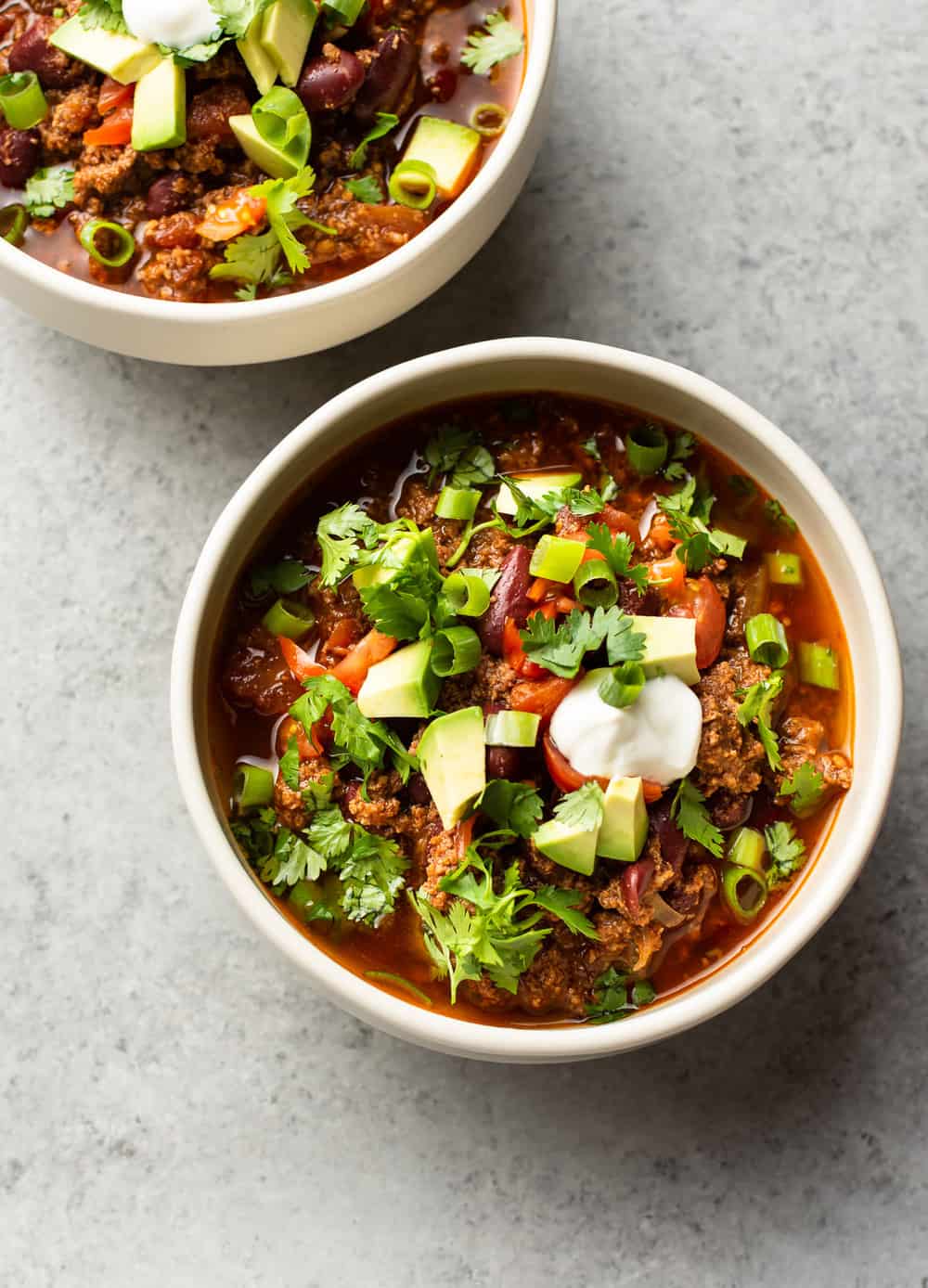 Instant Pot Chili is simple to make and hearty. The electric pressure cooker builds amazing flavors in a short time, and everyone will love loading up their bowls with their favorite toppings! Individual servings in small bowls, topped with avocado, sour cream, cilantro and green onions.