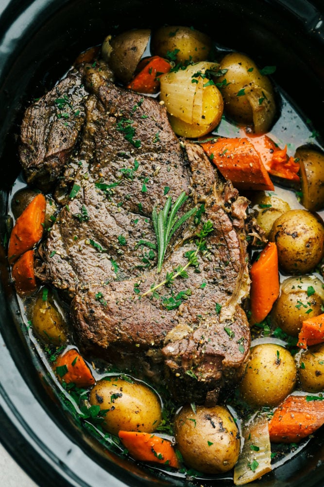 Fork-tender, melt-in-your-mouth pot roast with delicate potatoes and sweet carrots in a perfectly seasoned broth. This recipe is super simple but will make you feel like you've spent all day cooking. Top-down view of pot roast and vegetables in a slow cooker.