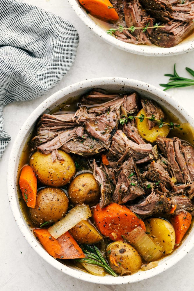 Fork-tender, melt-in-your-mouth pot roast with delicate potatoes and sweet carrots in a perfectly seasoned broth. This recipe is super simple but will make you feel like you've spent all day cooking. Shredded roast and vegetables served in a white bowl.