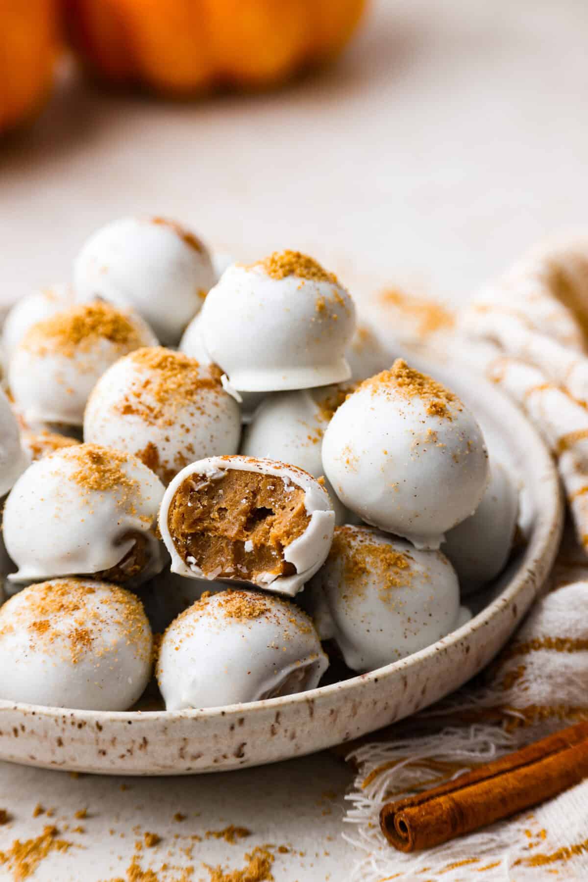 Pumpkin cream cheese truffles combine smooth cream cheese, pumpkin puree, crunchy graham cracker, and gingersnap crumbs, all dunked in sweet white chocolate. The best fall dessert. Side shot of a pile of pumpkin cream cheese truffles on a plate.