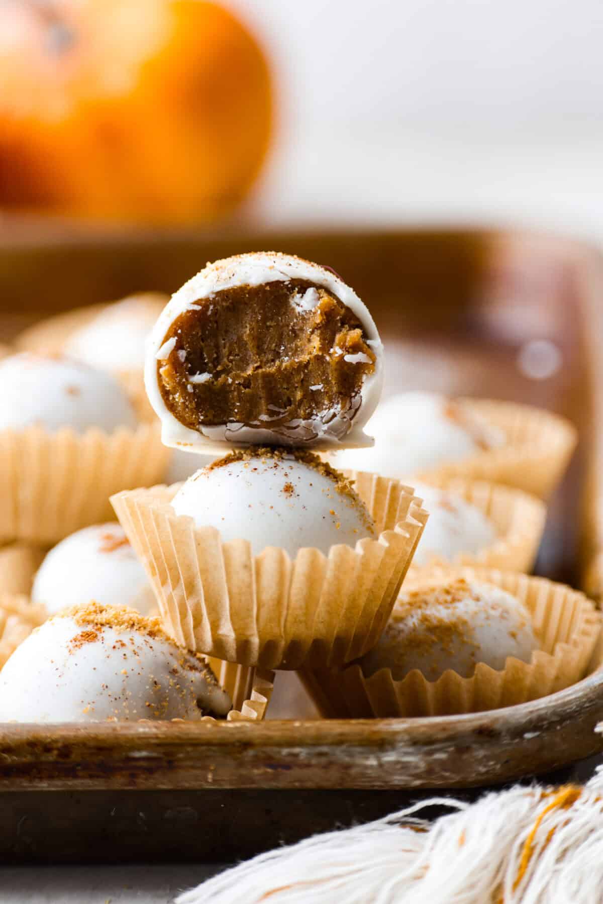 Pumpkin cream cheese truffles combine smooth cream cheese, pumpkin puree, crunchy graham cracker, and gingersnap crumbs, all dunked in sweet white chocolate. The best fall dessert. Close up shot of a pumpkin cream cheese truffle stacked on another truffle with a bite taken out of it.