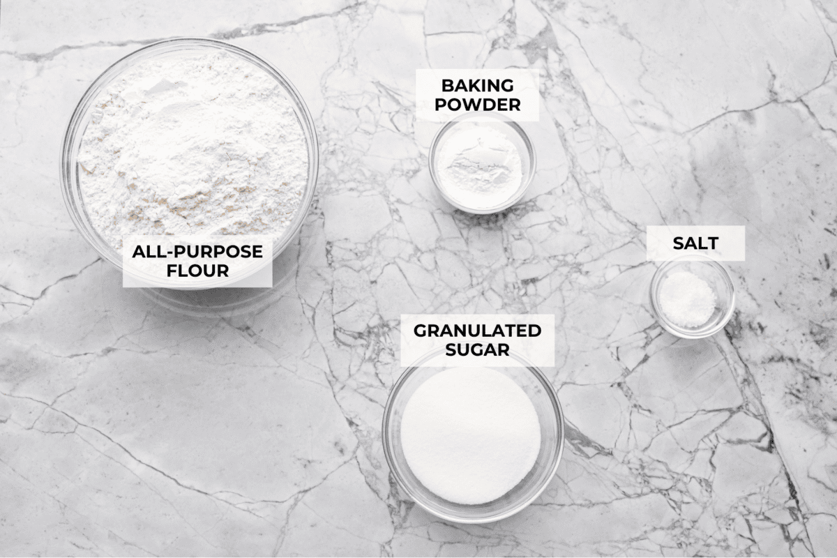 My Homemade Pancake Mix uses 4 pantry staple ingredients and 5 minutes to make! Ditch the box and whip up your mix for fluffy, delicate pancakes anytime! Overhead shot of labeled ingredients.