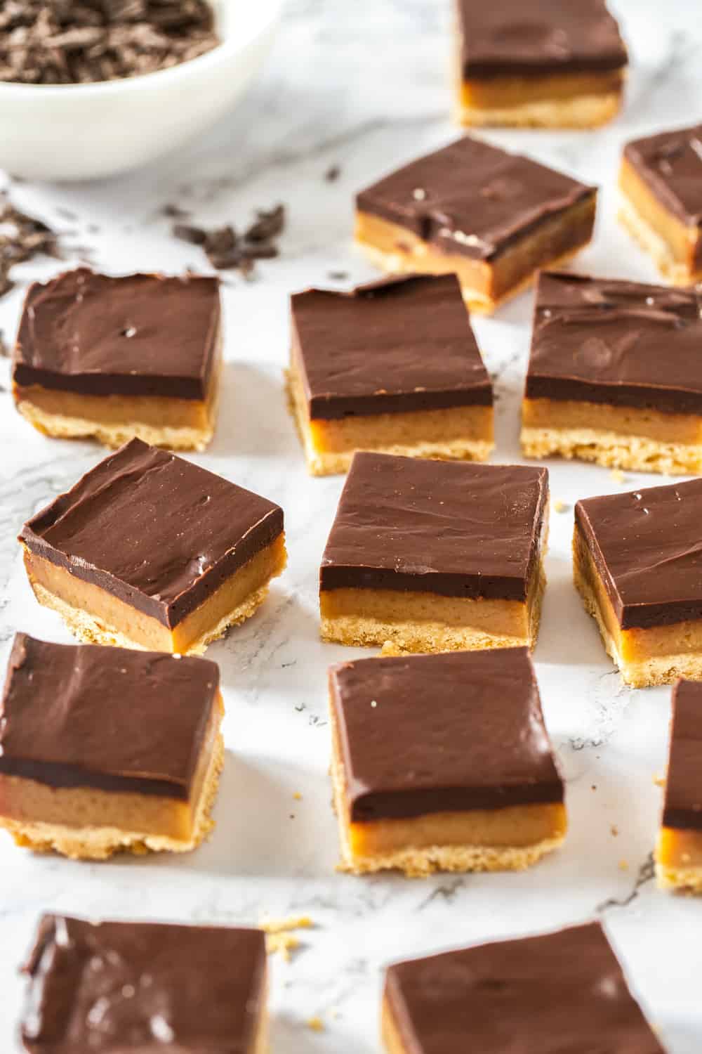 Three simple but indulgent layers make this Millionaire Shortbread recipe a winner every time. Just 8 every day ingredients magically turn into a crispy shortbread base, soft and chewy caramel centre and a rich and thick layer of chocolate ganache. Close up of a batch of sliced up millionaire shortbread