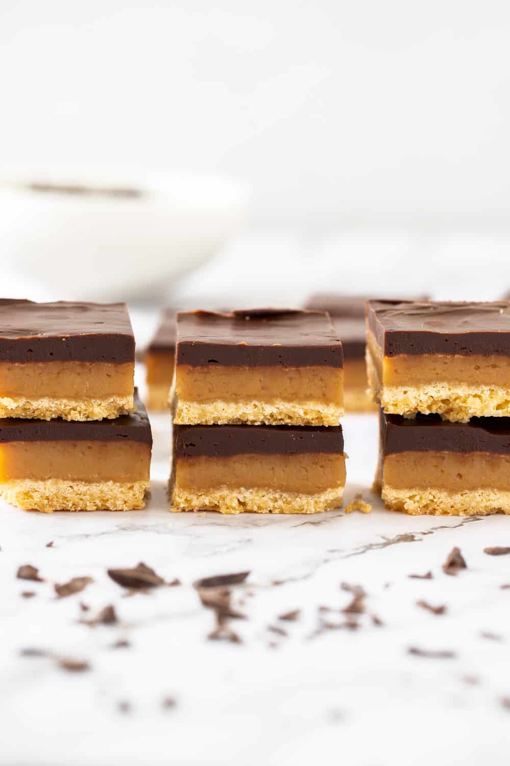 Three simple but indulgent layers make this Millionaire Shortbread recipe a winner every time. Just 8 every day ingredients magically turn into a crispy shortbread base, soft and chewy caramel centre and a rich and thick layer of chocolate ganache. 3 stacks, each with 2 pieces of millionaire shortbread. Chocolate scattered in front