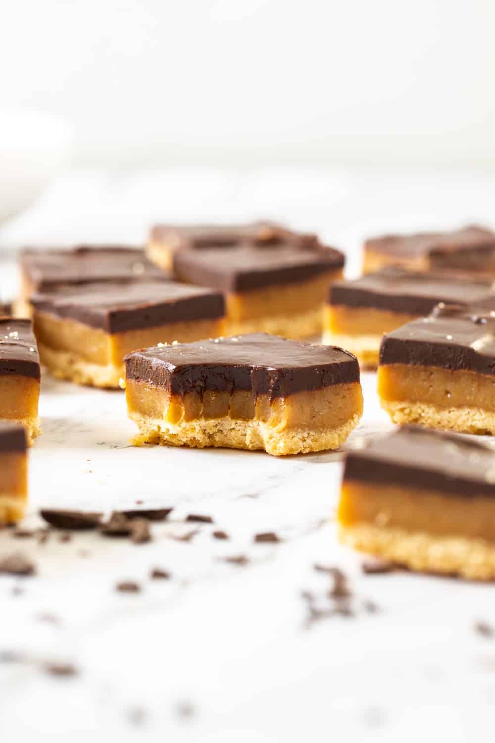 Three simple but indulgent layers make this Millionaire Shortbread recipe a winner every time. Just 8 every day ingredients magically turn into a crispy shortbread base, soft and chewy caramel centre and a rich and thick layer of chocolate ganache. Closeup of a slice of millionaire shortbread with a bite mark in it