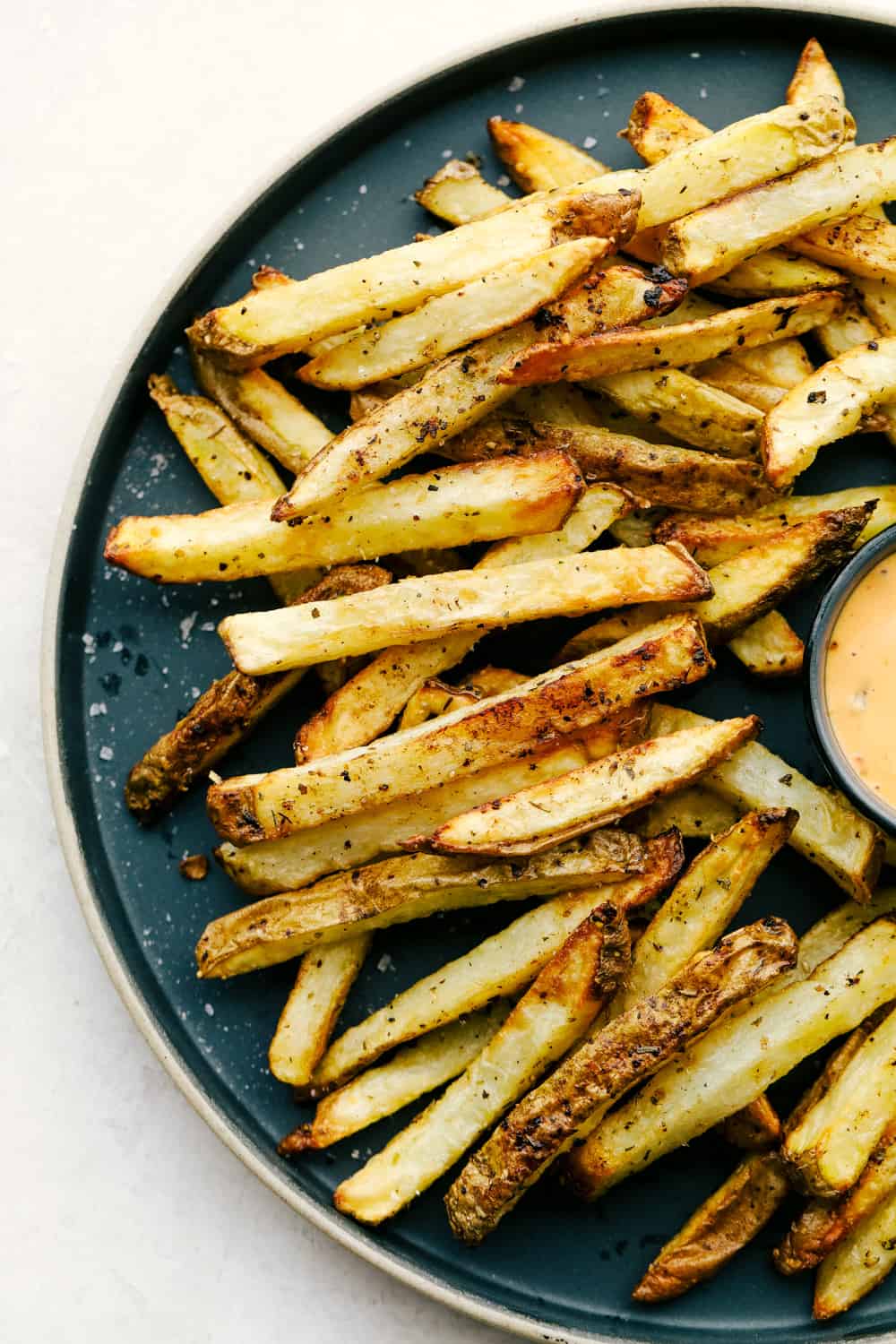Air Fryer French Fries have a perfectly crispy outside, tender inside, and are absolutely heavenly. Super easy to make, too! You won't believe that these fries aren't deep-fried are after you try one. They almost taste too good to be true! Air fryer French fries served on a black plate with a creamy dipping sauce.