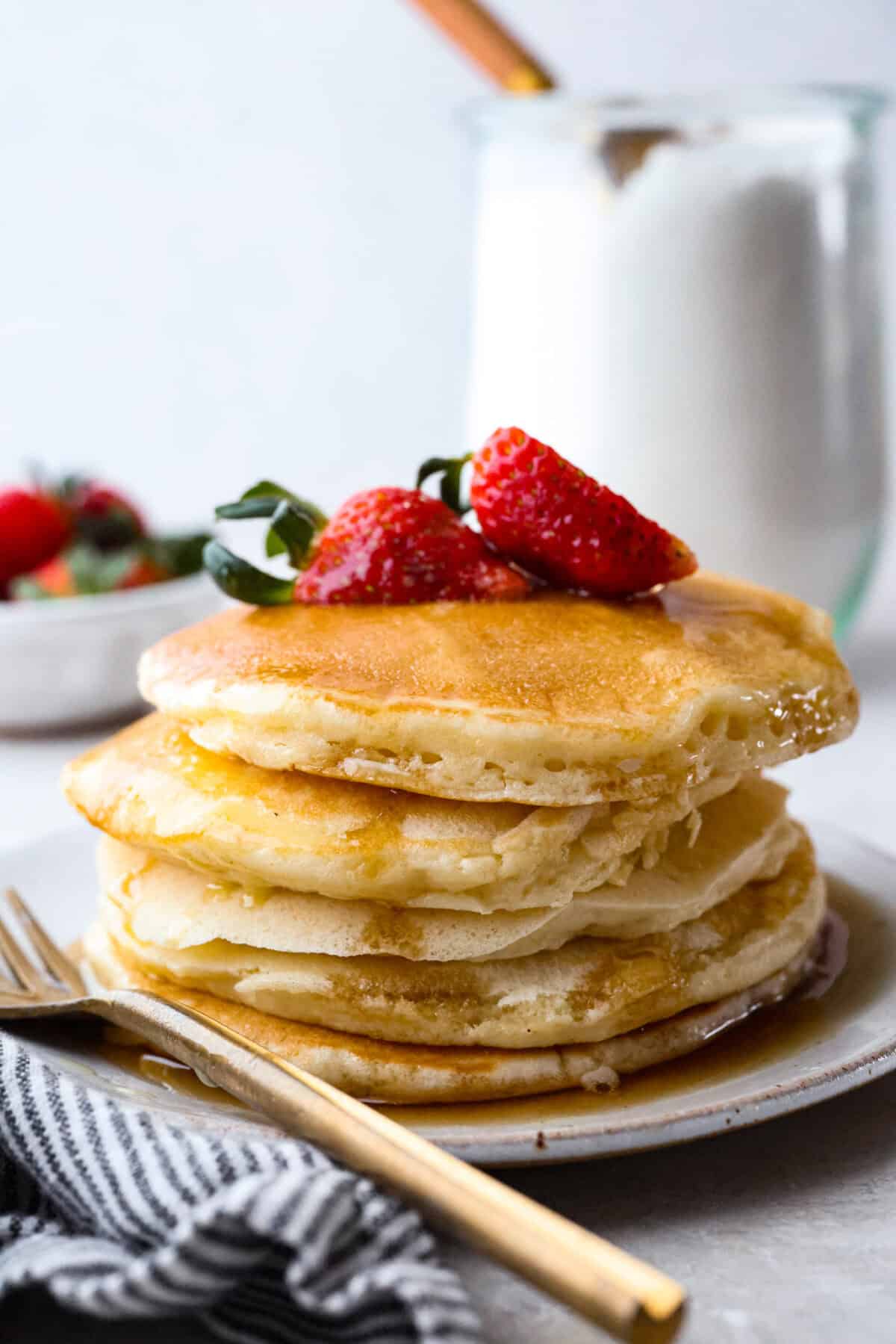 My Homemade Pancake Mix uses 4 pantry staple ingredients and 5 minutes to make! Ditch the box and whip up your mix for fluffy, delicate pancakes anytime! Close up shot of a pack of pancakes made from my homemade pancake mix, with strawberries on top.