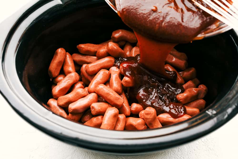 Little Smokies, smothered in a sweet tangy BBQ sauce are one of the easiest, most loved appetizers out there. These are guaranteed to disappear whether it's for a party or dinner, these are just too tasty and fun not to eat. Sauce being poured over little smokies in the slow cooker.