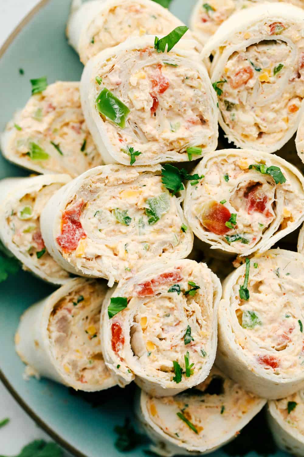 Mexican Pinwheels are a slightly spiced creamy chicken blend rolled up in easy to eat bite sized pinwheels. Soft pillowy tortillas wrapped around colorful, amazing flavored filling are going to be a hit at your next gathering! Pinwheels stacked on top of each other on a plate.