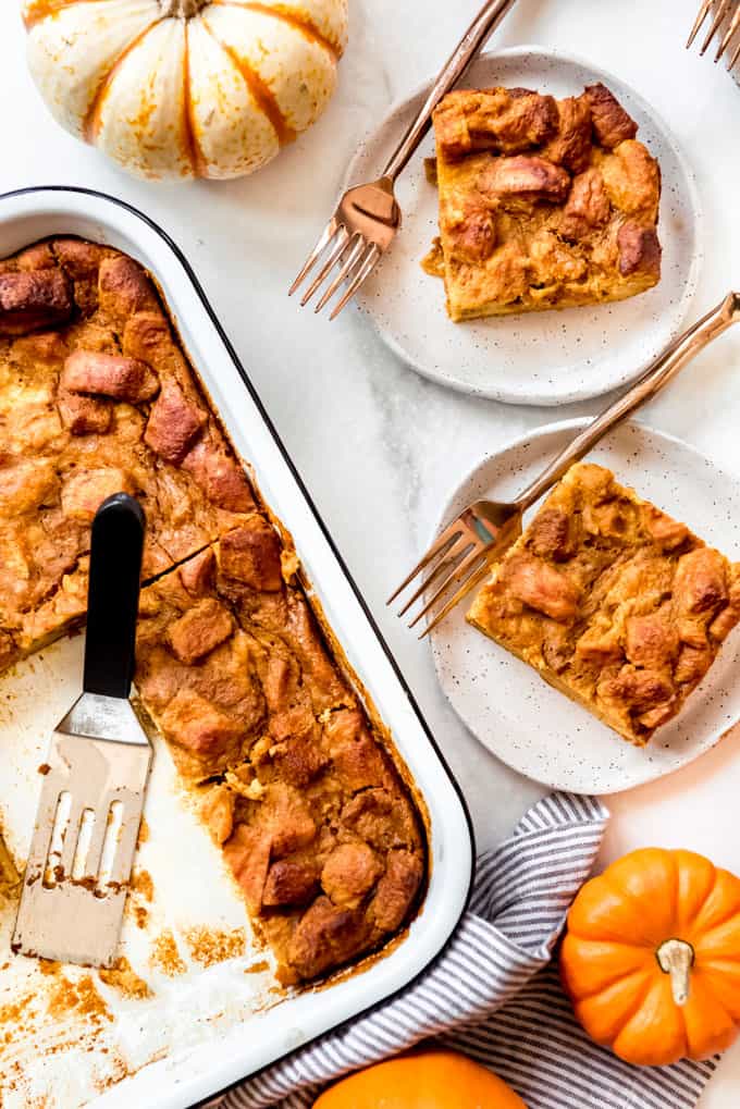 Pumpkin Bread Pudding is an easy and fantastic recipe that tastes like you have spent a lot of time putting it together when it really only takes minutes! Drizzle warm slices with caramel sauce and serve it with ice cream for a decadent dessert, or even enjoy it for breakfast like a baked french toast casserole! Slices of bread pudding on plates with forks next to small pumpkins.