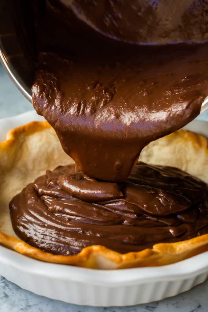 Chocolate Pie has an easy, homemade chocolate pudding that is the perfect pie filling! Smooth and creamy chocolate layered with sweet, vanilla whipped cream is the perfect dessert.ย Chocolate pudding being poured in a baked pie crust.
