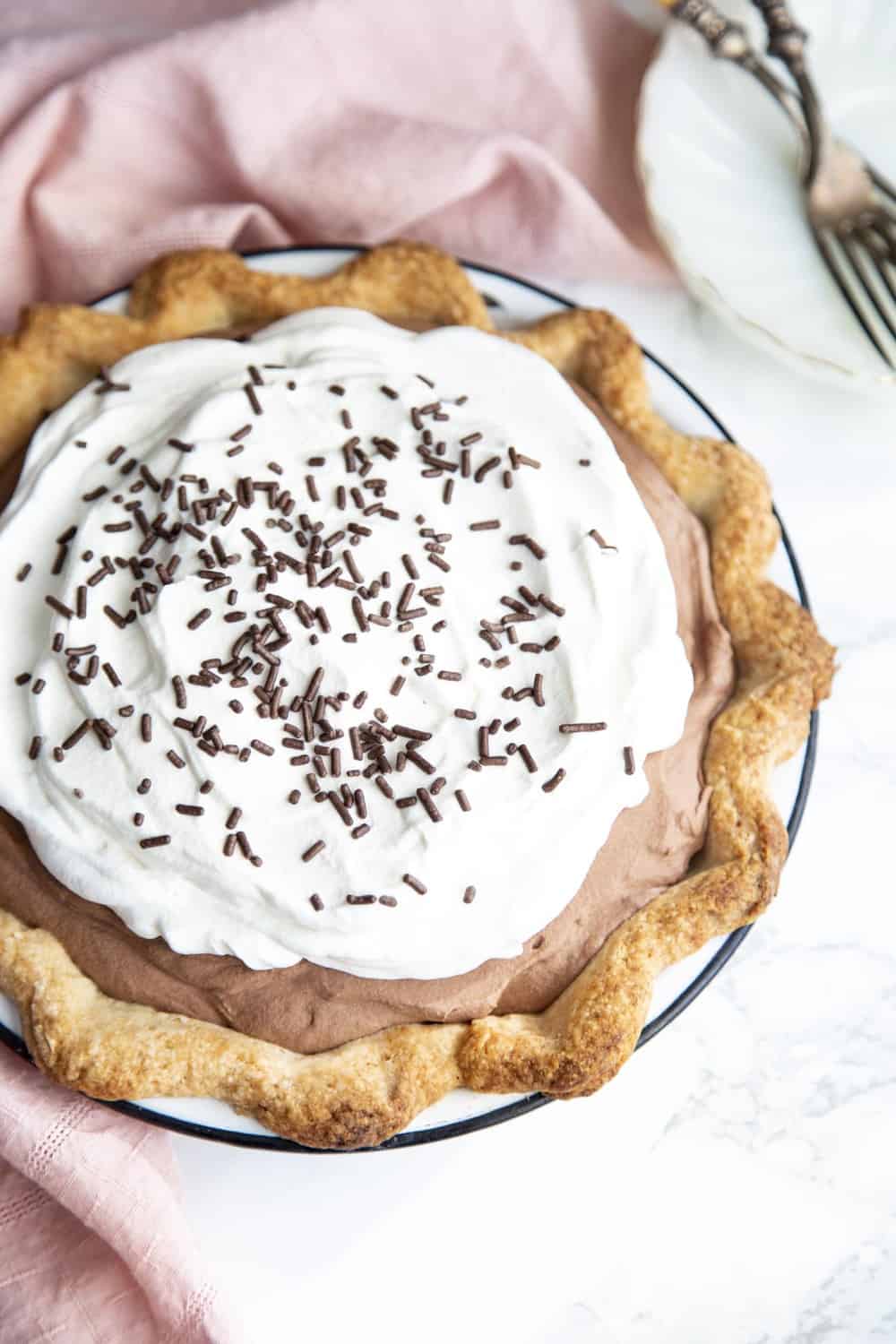 A flakey crust is filled with a decadent, dreamy, creamy, chocolate filling and topped with pillows of cream for this irresistible French Silk Pie. The filling is so smooth and rich, and then encased in a buttery crust. French Silk pie with whipped topping and chocolate sprinkles.