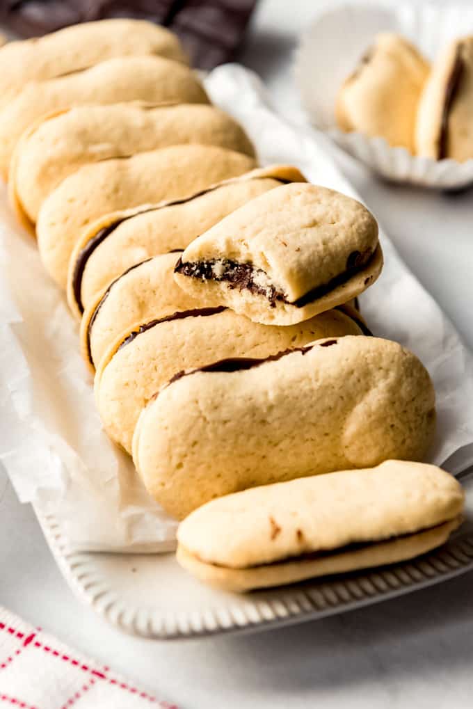 Homemade Milano Cookies have tender cookies with a nice crunch sandwiched around a layer of rich dark chocolate in the center! They taste even better than the store bought version! Milano cookies staked together on a white dish.