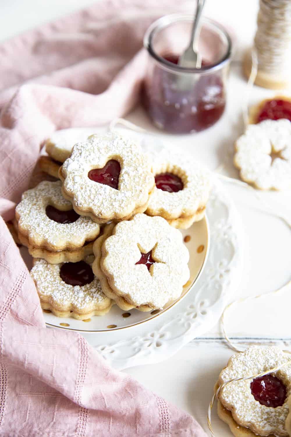 Linzer cookies are a combination of buttery orange infused shortbread and jam, as pleasing to look at as they are to eat. These festive treats are perfect for any holiday or special occasion. Cookies stack on top of each other on a white plate.