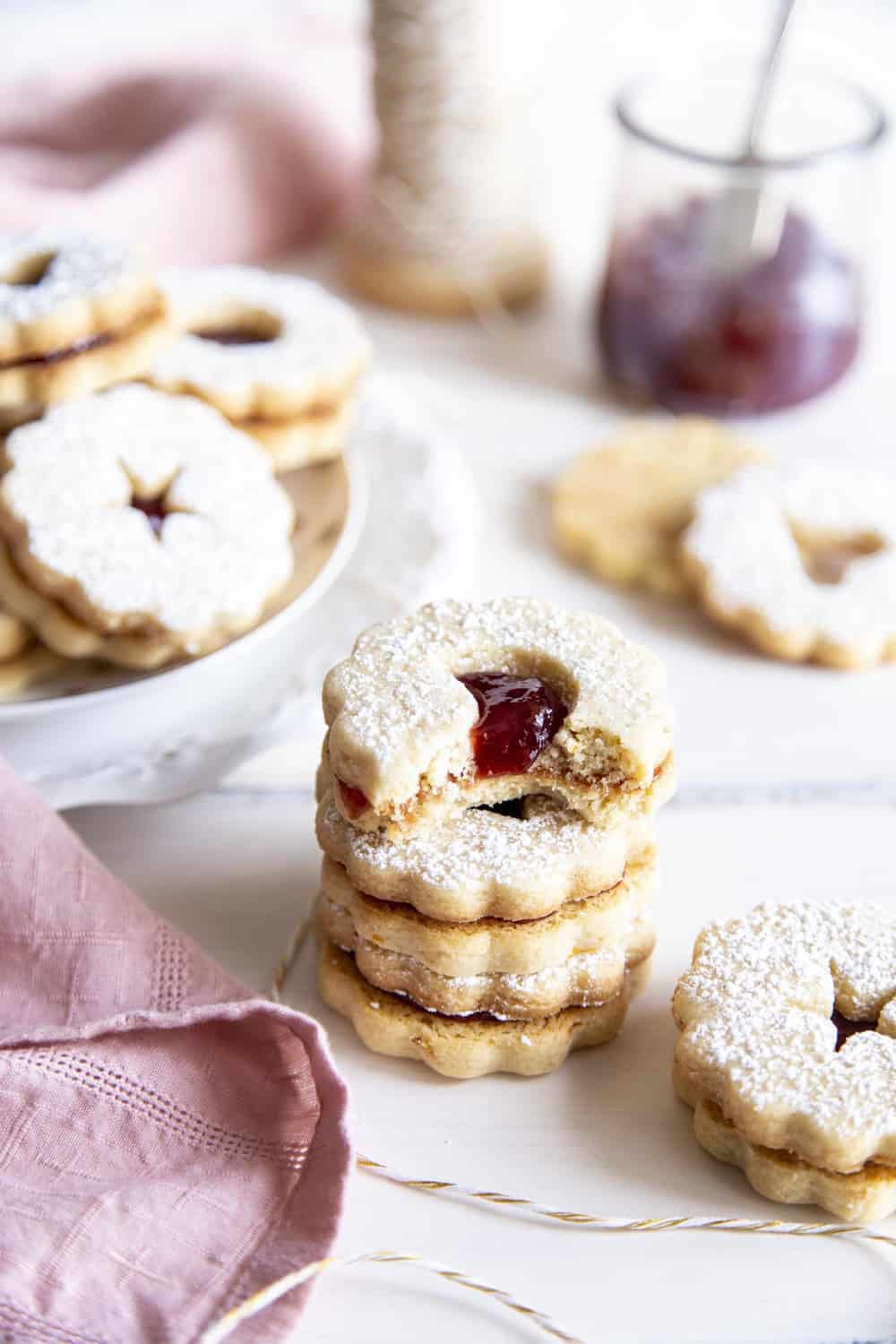 Linzer cookies are a combination of buttery orange infused shortbread and jam, as pleasing to look at as they are to eat. These festive treats are perfect for any holiday or special occasion. A stack of Linzer Cookies with a bite out of it.